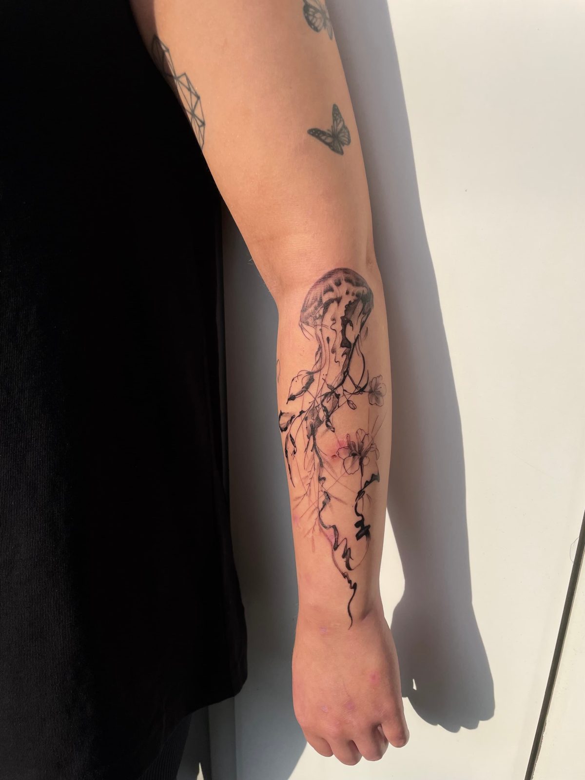 Abstraktes Tattoo einer Qualle mit floralen Ranken am Unterarm